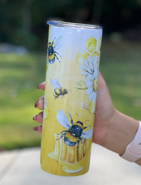 honey bee tumbler, an ombre white to honey colored tumbler with bees in flight and sitting on a honey dipper, with daisies