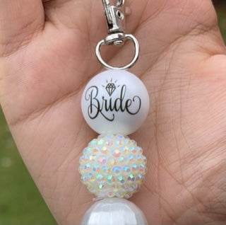 Close up: This keyring is made of three 22mm acrylic beads, the first has the Bride in an elegant font with the "i" doted with a diamond, the second is a rhinestone bead, the third bead is a textured pearlescent finish all off by a silver capped white tassel. This would be a great way to give to your heart to a love one.