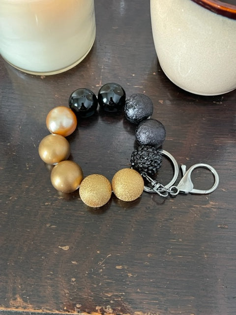 This bracelet features ten 20mm acrylic beads . It features 5 black beads one being a rhinestone bead and 5 gold beads, and a silver swivel keyring with a large lobster claps.