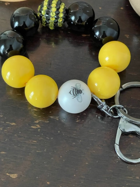Close up. This bracelet features ten 20mm bubble gum beads with with two feature beads one yellow and black rhinestone bead and one with a bumble bee. The other 8 beads are 4 black and 4 yellow, with clasp is a silver swivel lobster clasp keyring.