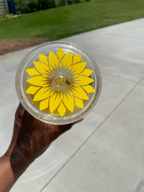 Acrylic lid to a cup decorated with the petals of a yellow sunflower .