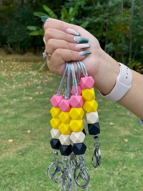 This is a pencil lanyard with one pink silicone, 2 yellow, one tan and one black silicon beads, with  swivel keyring clasp attached to the end. 