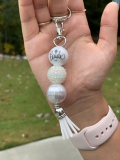 This keyring is made of three 22mm acrylic beads, the first has the Bride in an elegant font with the "i" doted with a diamond, the second is a rhinestone bead, the third bead is a textured pearlescent finish all off by a silver capped white tassel. This would be a great way to give to your heart to a love one.