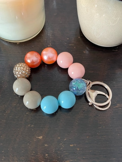 This bracelet features ten 20mm acrylic beads arranged the beads are light blue, tan and coral. It's features a rose gold swivel keyring with a large lobster claps.