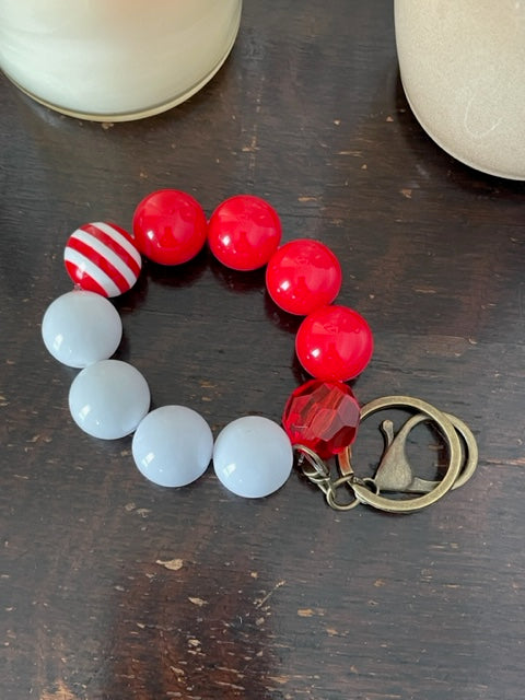 This bracelet features ten 20mm acrylic beads arranged the beads are 4 read beads one red and white striped beads 3 red beads and 1 clear facetted red bead for a total of 10 beads. It's features a bronze swivel keyring with a large lobster claps.