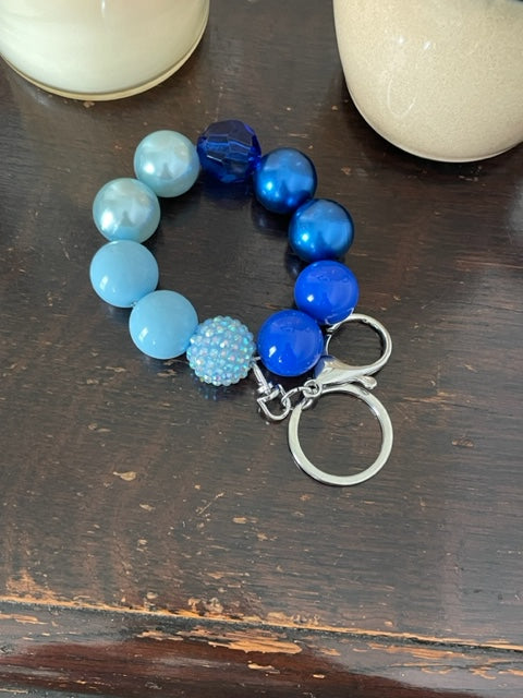 This bracelet features ten 20mm acrylic beads . It features  blue ombre beads with one rhinestone bead, one clear blue facetted bead and a silver swivel keyring with a large lobster claps.