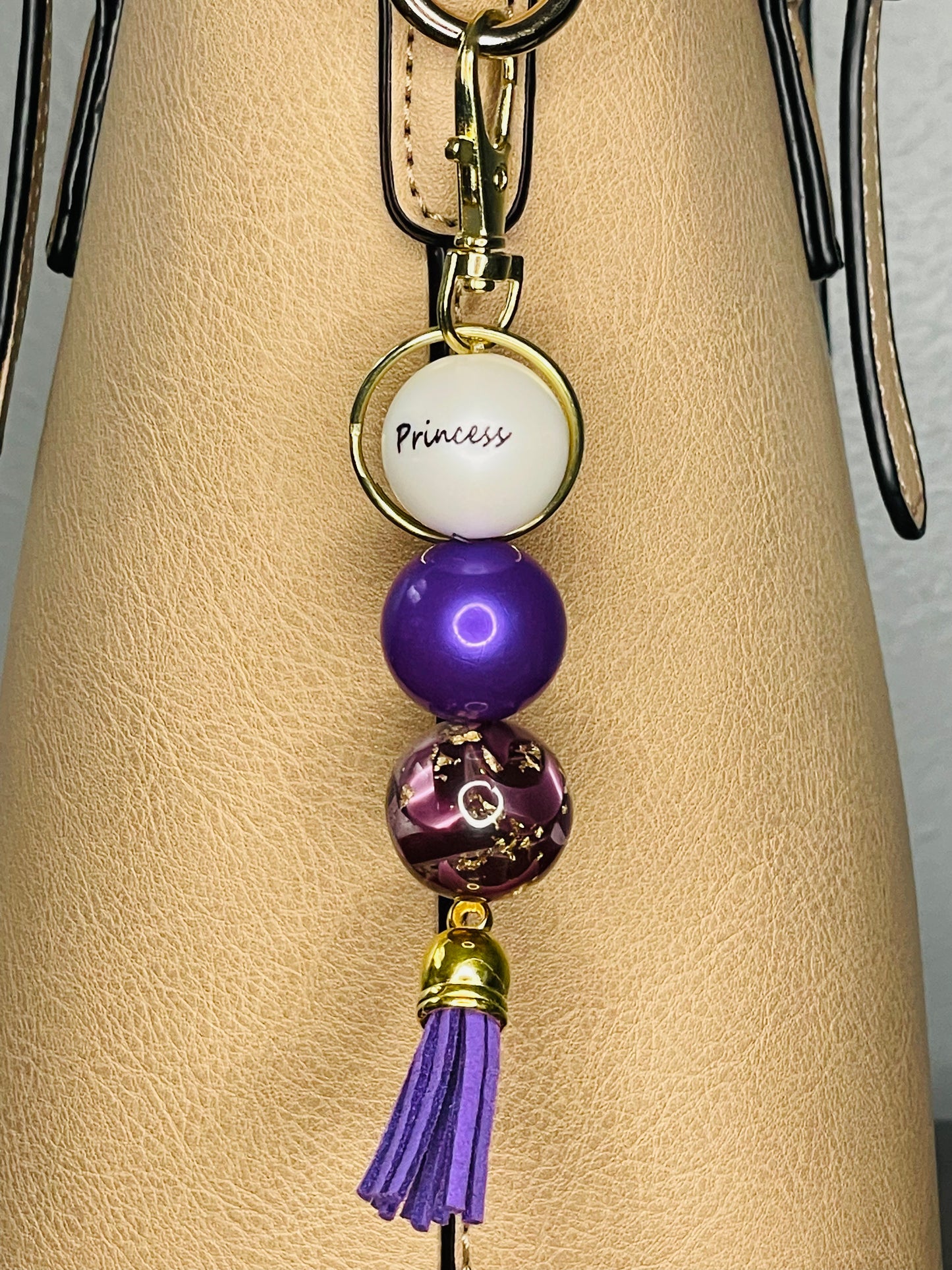 A key ring on a gold ring with 3 beads the first white with Princess written on the bead, is a deep shiny purple , the third a  shiny gold fleck and purple swirled. The key chain is finished with a urple tassel.