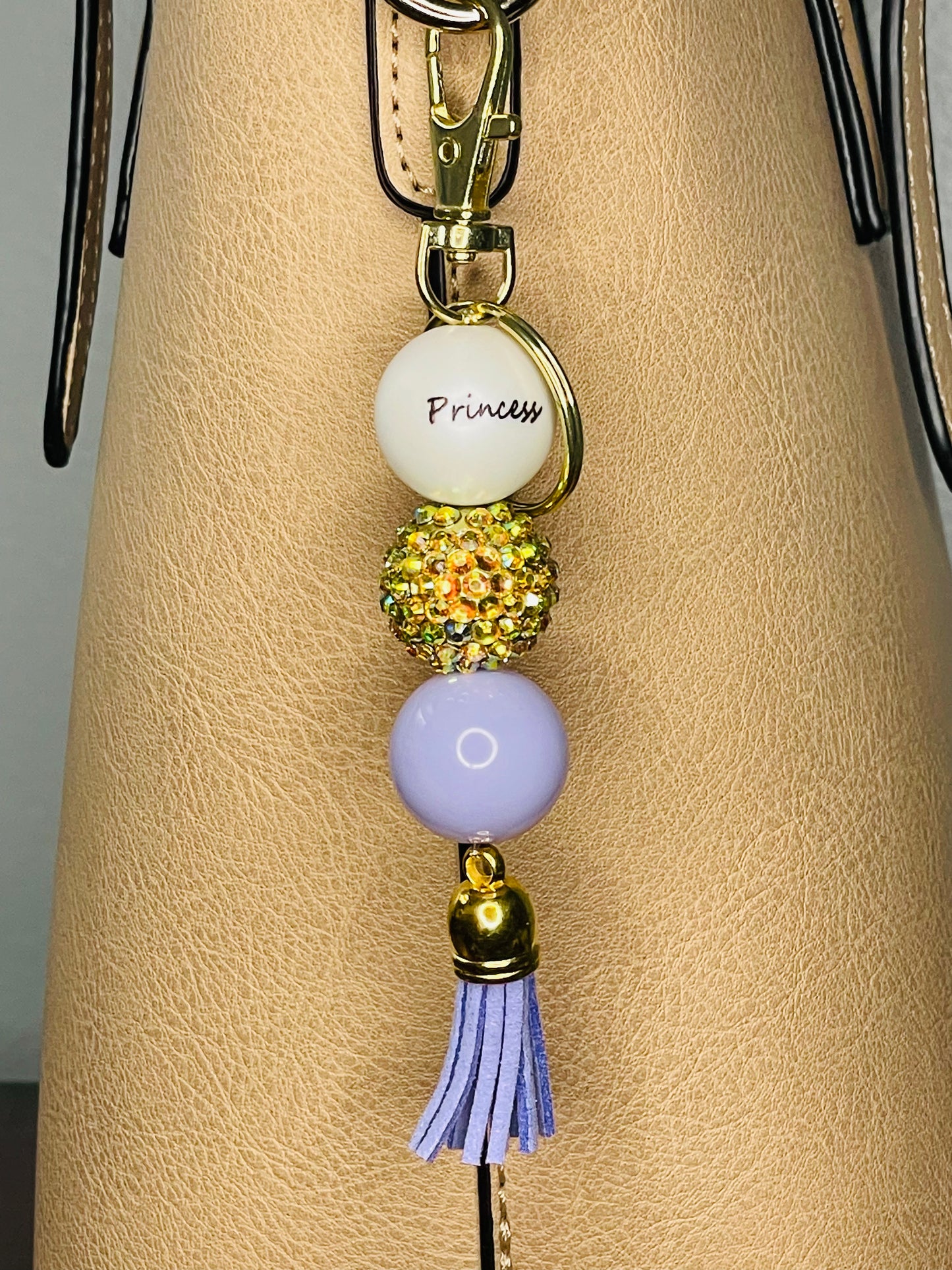 A key ring on a gold ring with 3 beads the first white with Princess written on the bead, is  Gold Rhinestone , the third a light purple. The key chain is finished with a light purple tassel